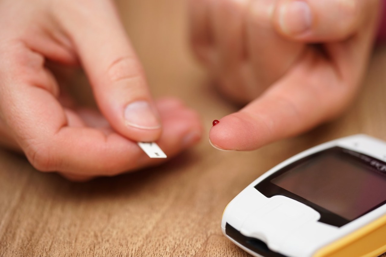 Blutzuckermessung bei Diabetes. Patient hat Bluttropfen am Finger. Teststreifen und Messgerät sind einsatzbereit.