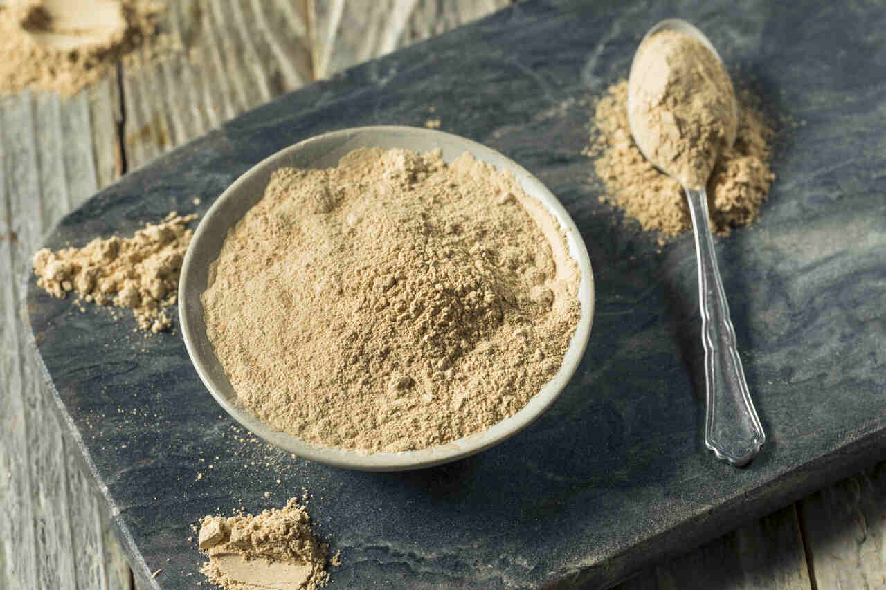 Gelbes Maca-Pulver in einer Schüssel und auf einem Löffel.