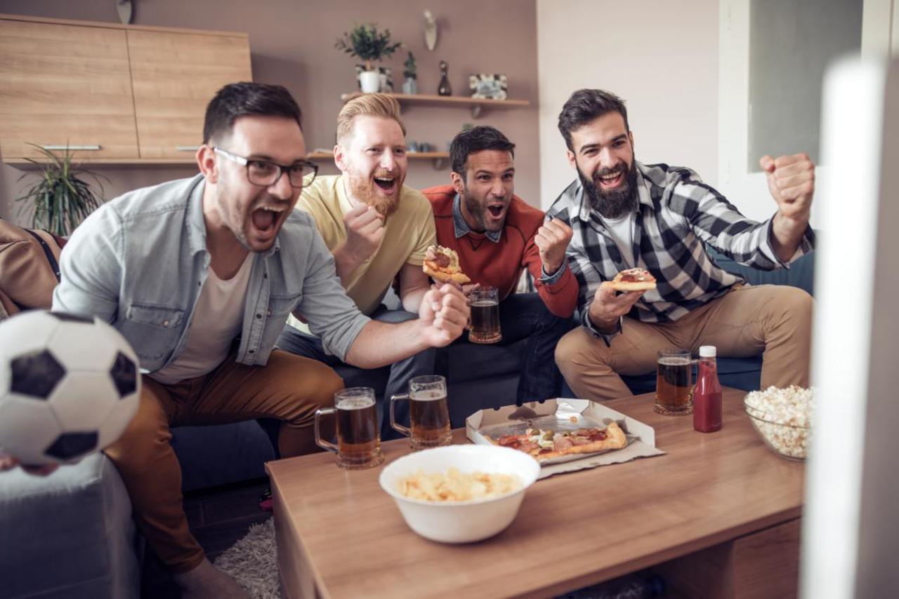 Fußball-Fans gucken zu Hause zusammen ein Spiel. Sie jubeln weil die Mannschaft gewinnt.
