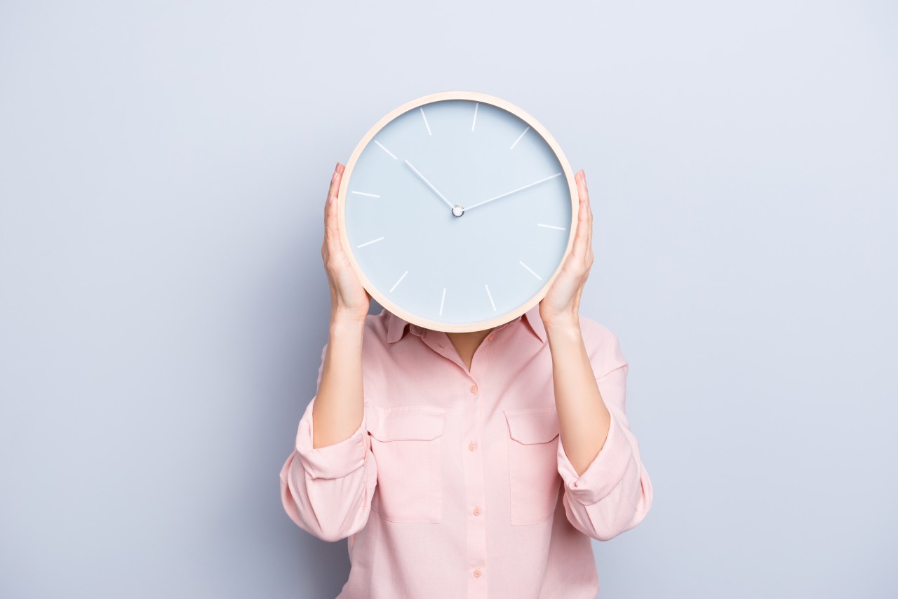 Frau bedeckt Kopf mit Uhr auf grauem Hintergrund.