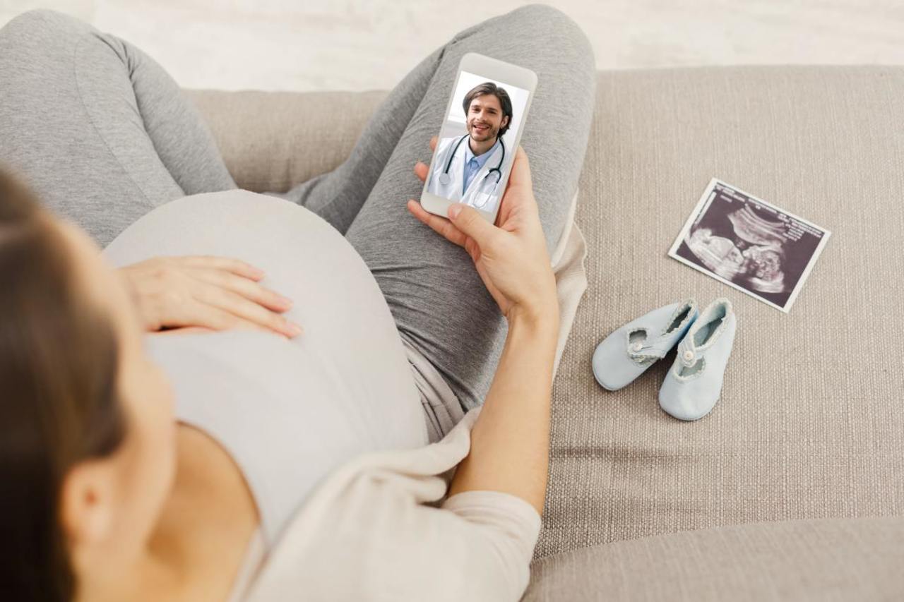 Schwangere Frau nutzt Telemedizin Videosprechstunde online auf ihrem Smartphone, Gespräch mit Frauenarzt.