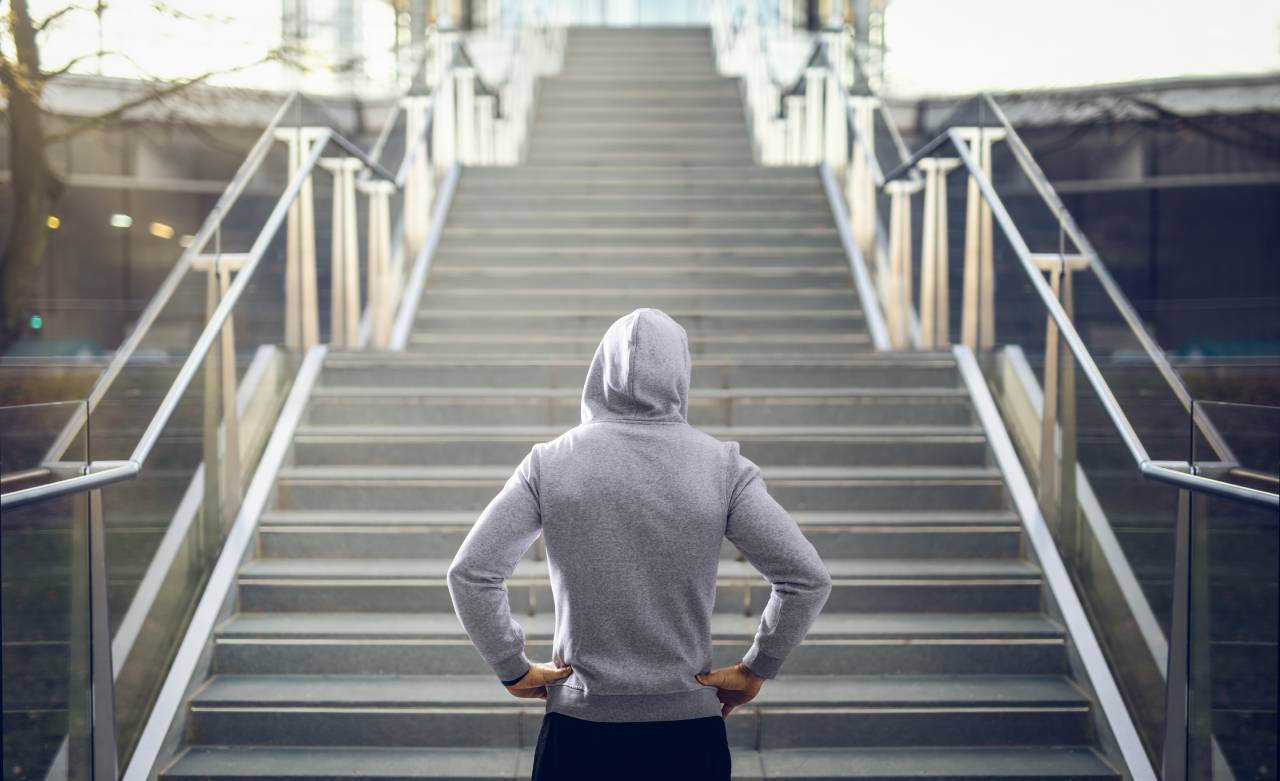 Ein Mann im grauen Kapuzenpullover steht vor einer Treppe.