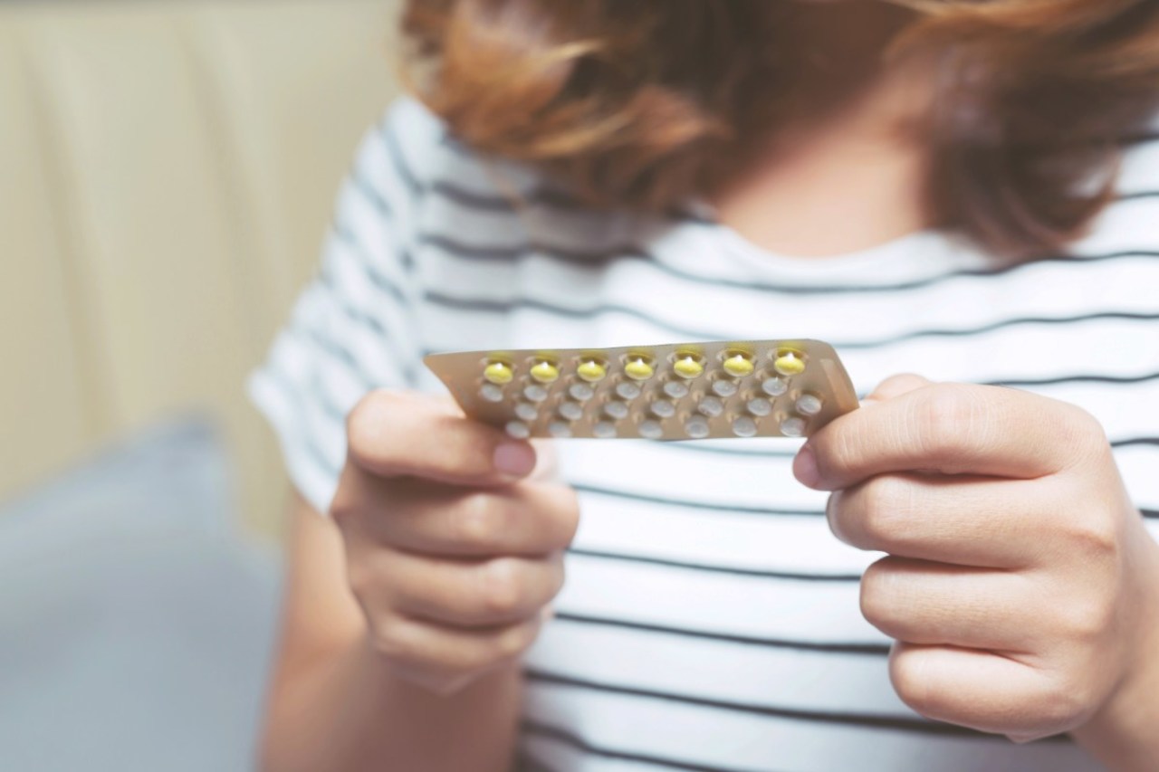 Frau hält Antibabypille in der Hand, Hormone können zu Haarausfall führen.