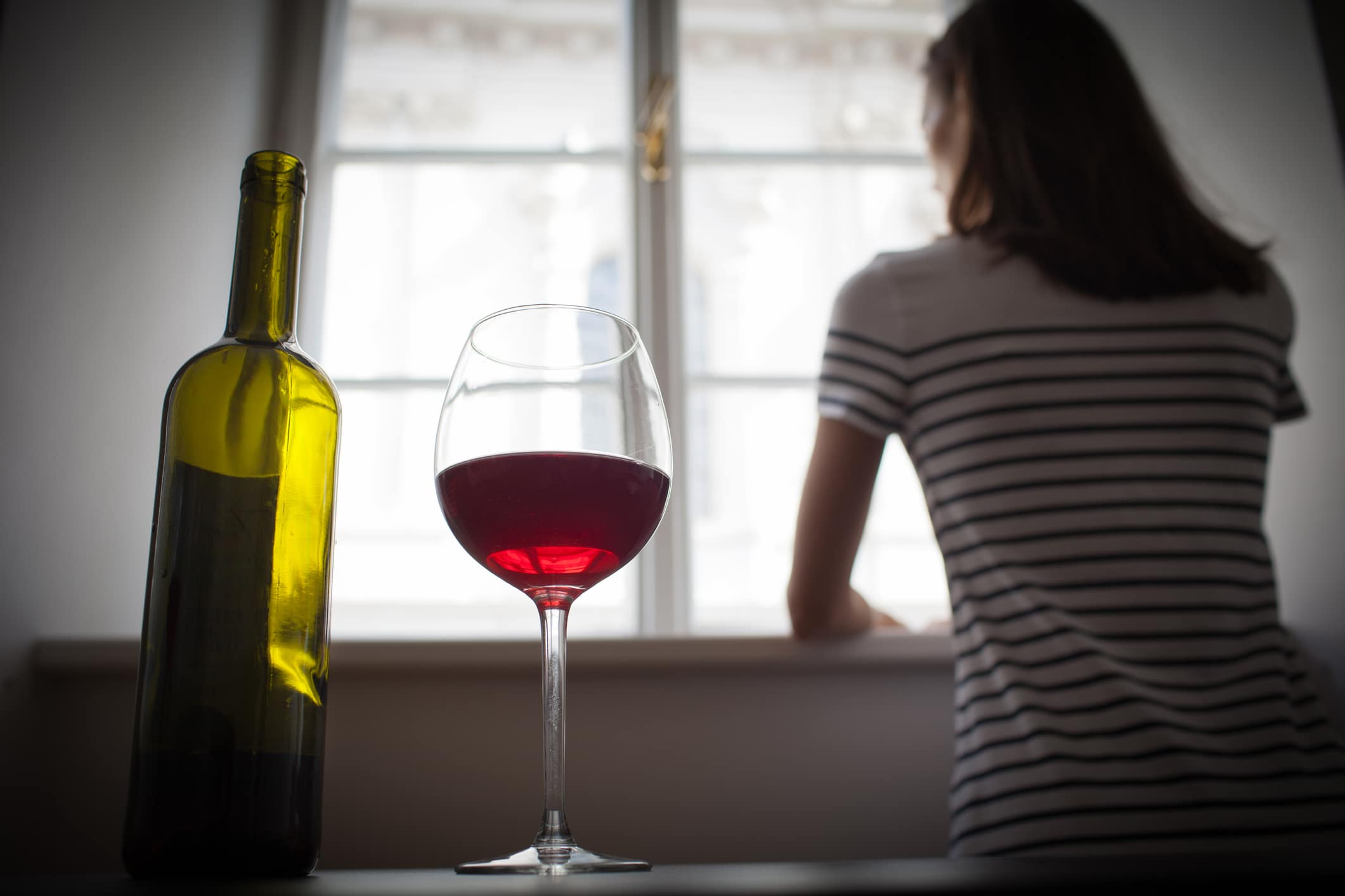 Flasche und Glas Rotwein mit Frau im Hintergrund