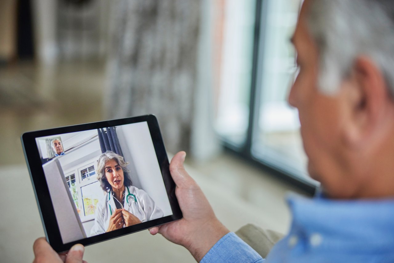Ein älterer Mann nimmt mit einem Tablet an der Online-Sprechstunde einer Ärztin teil.