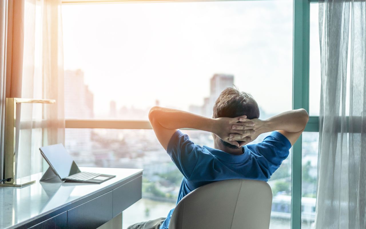 Mann im Büro lehnt sich im Stuhl zurück und blickt in die Skyline.