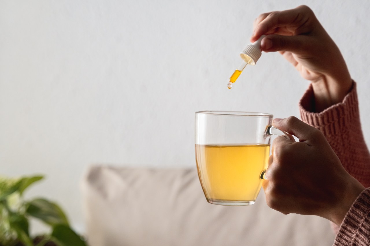 Hände geben mit einer Pipette Cannabis-Öl in eine Tasse Tee.
