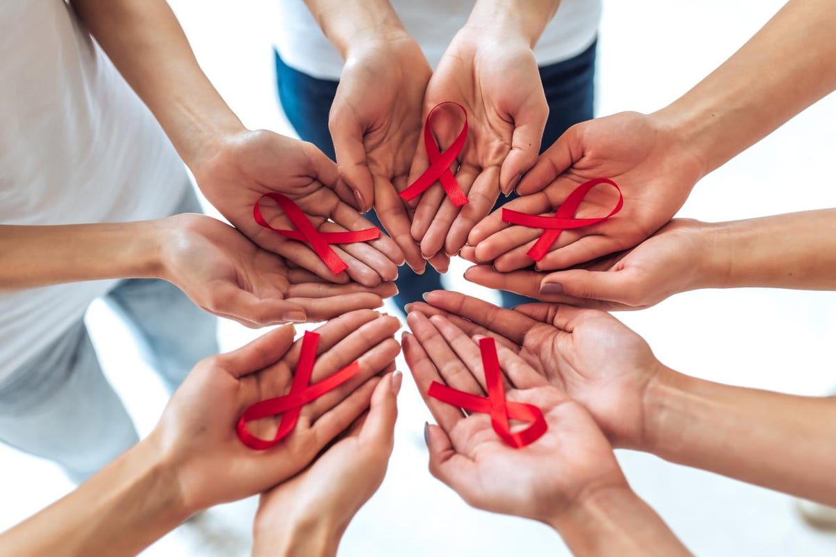 Zum Welt AIDS Tag: Solidarität mit den Betroffenen. Viele Hände halten rote Schleifen.