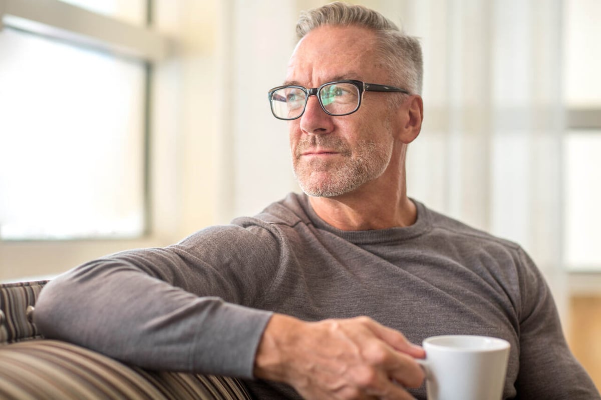 Ein Mann mittleren Alters sitzt mit einer Kaffeetasse auf dem Sofa.