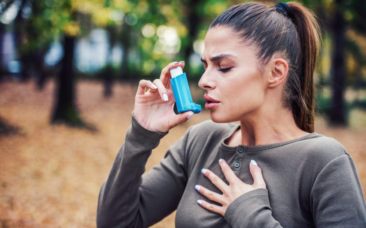 Eine junge Frau steht im Wald und benutzt Asthmaspray.