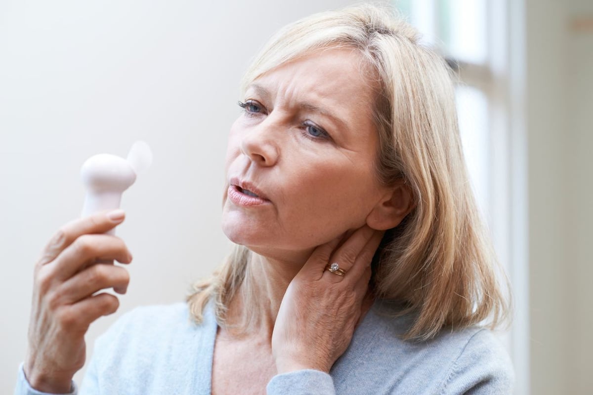 Hormonersatztherapie (HET). Frau mit Hitzewallungen hält Ventilator.