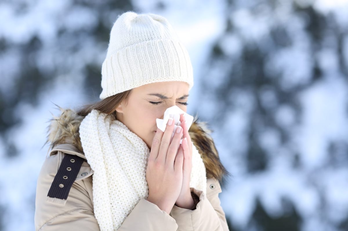 Eine Frau mit winterlicher Kleidung und Schnee im Hintergrund putzt sich die Nase.