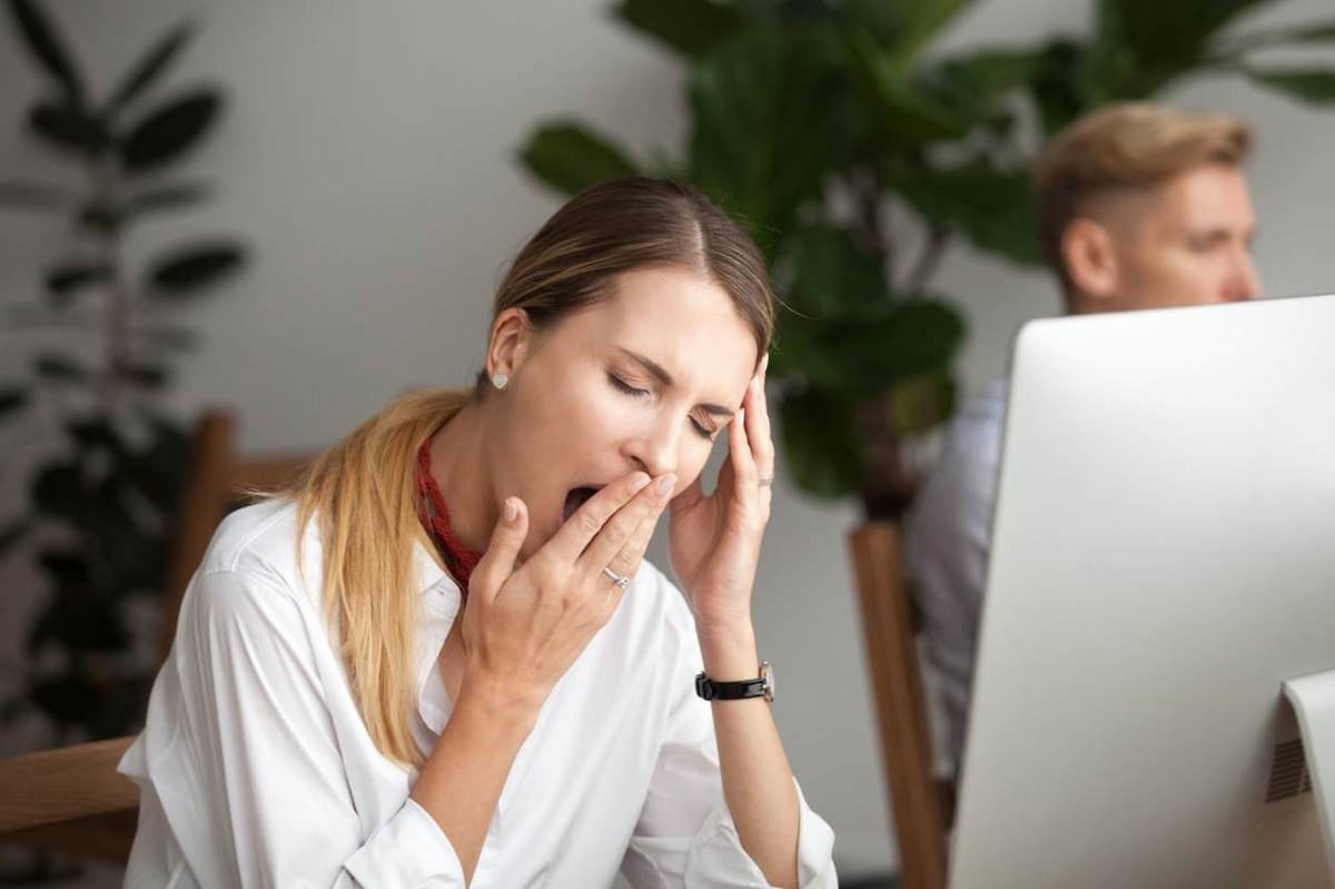 Eine Frau ist müde im Büro und gähnt an ihrem Schreibtisch am Laptop.
