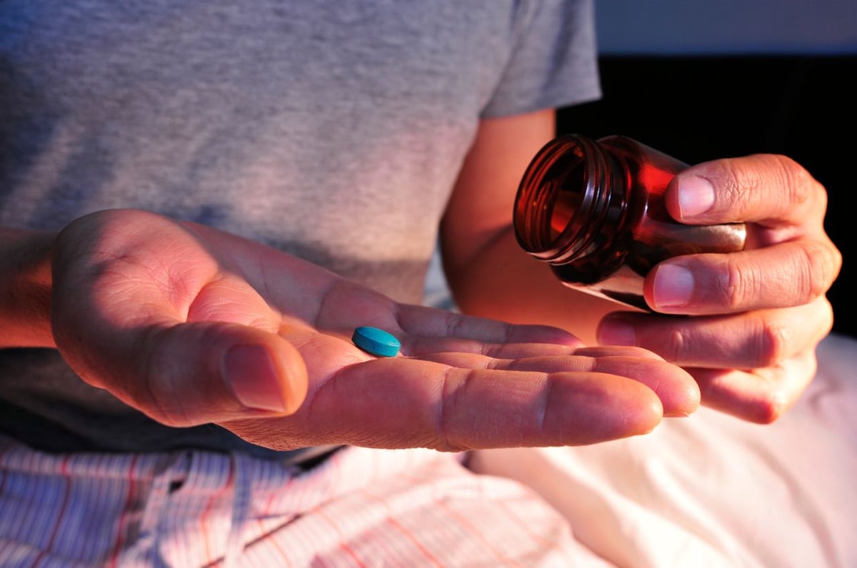 Aus einer Glasflasche schüttet ein Mann sich eine blaue Tablette auf die Handfläche.