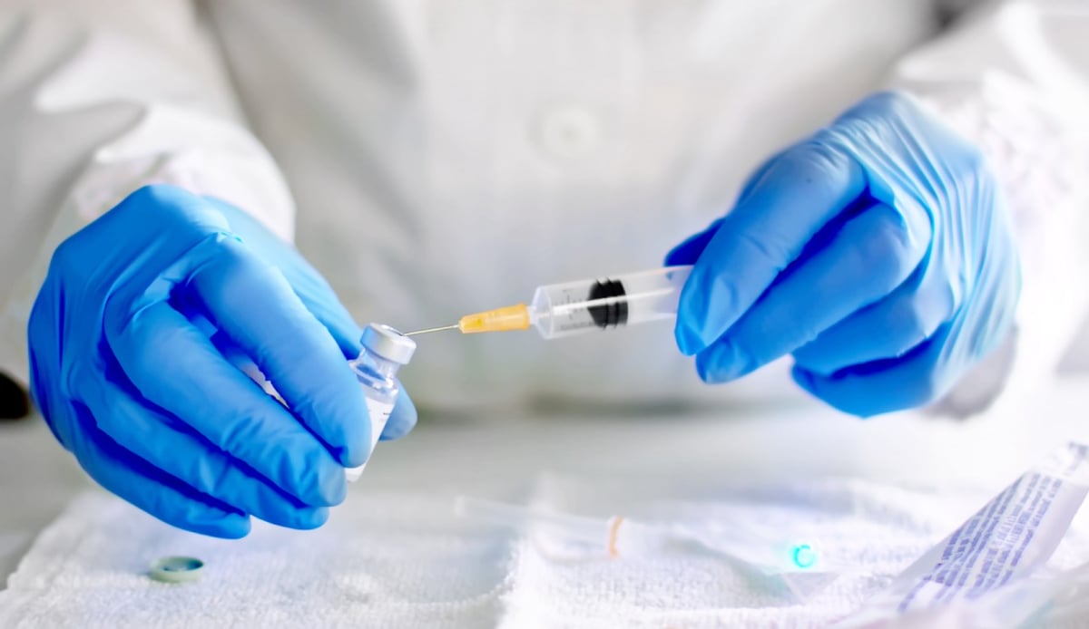 Hände mit blauen Handschuhen bereiten eine Spritze mit Impfstoff vor.