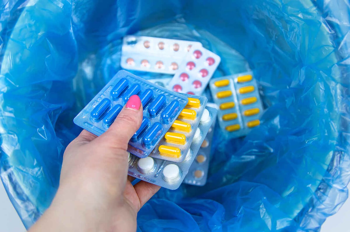 Eine Frauenhand wirft mehrere Tabletten in einen Mülleimer.