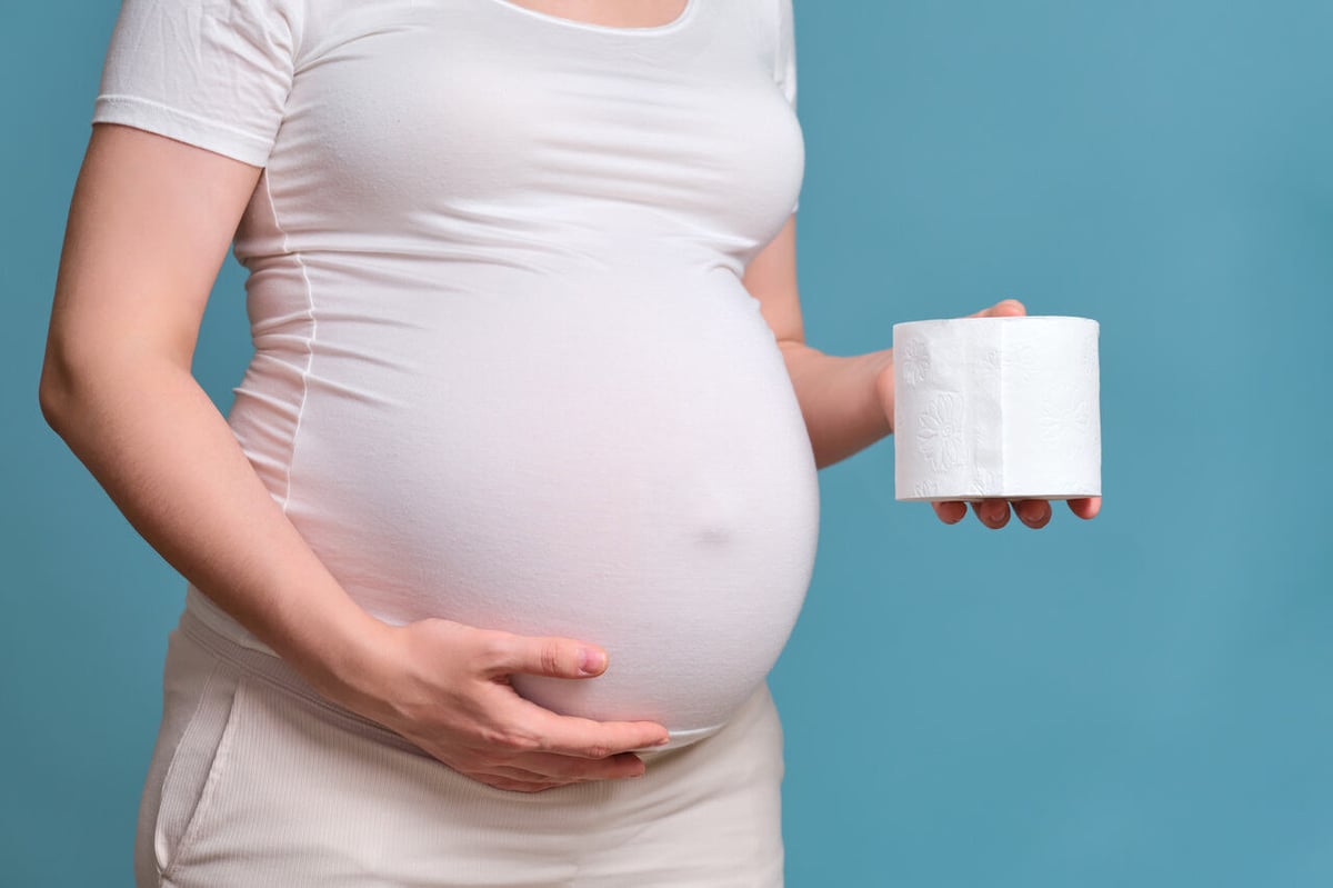 Hämorrhoiden in der Schwangerschaft: Hochschwangere Frau hält eine Rolle Klopapier neben ihrem Bauch.