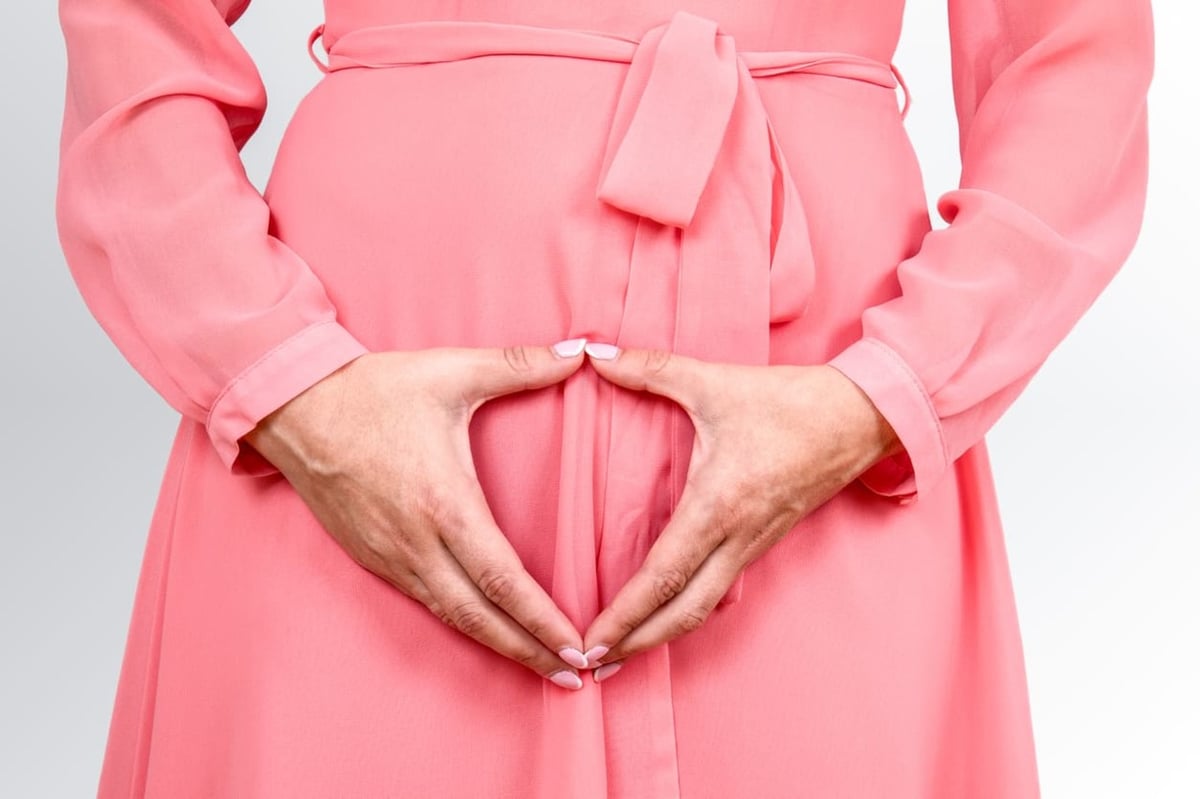 Frau im Kleid hält Hände vor das Becken.