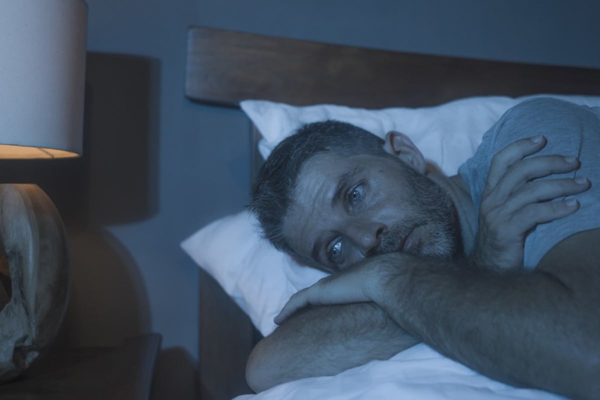 Ein Mann liegt in einem abgedunkelten Raum schlaflos im Bett.