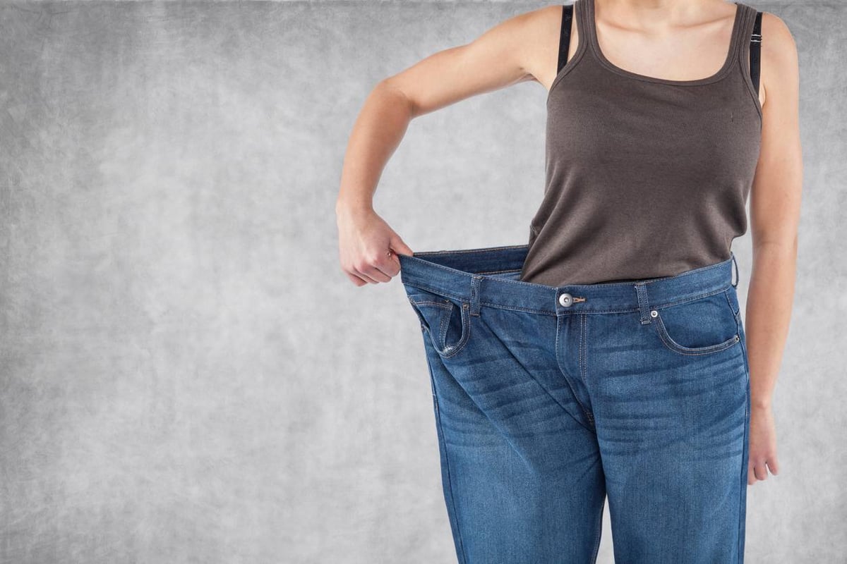Frau hält zu große Jeanshose mit einer Hand an der Hüfte.
