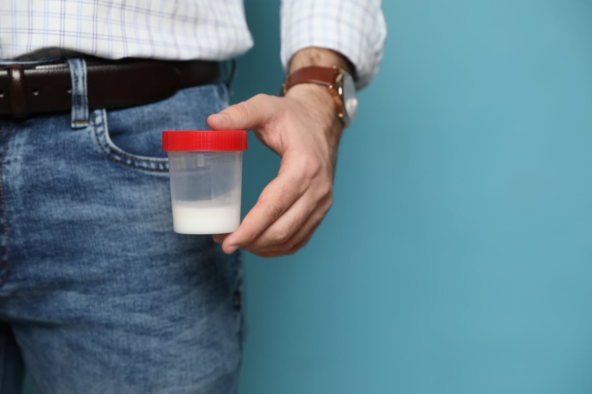 Ein Mann hält eine Samenspende oder Spermaprobe in einem Becher.