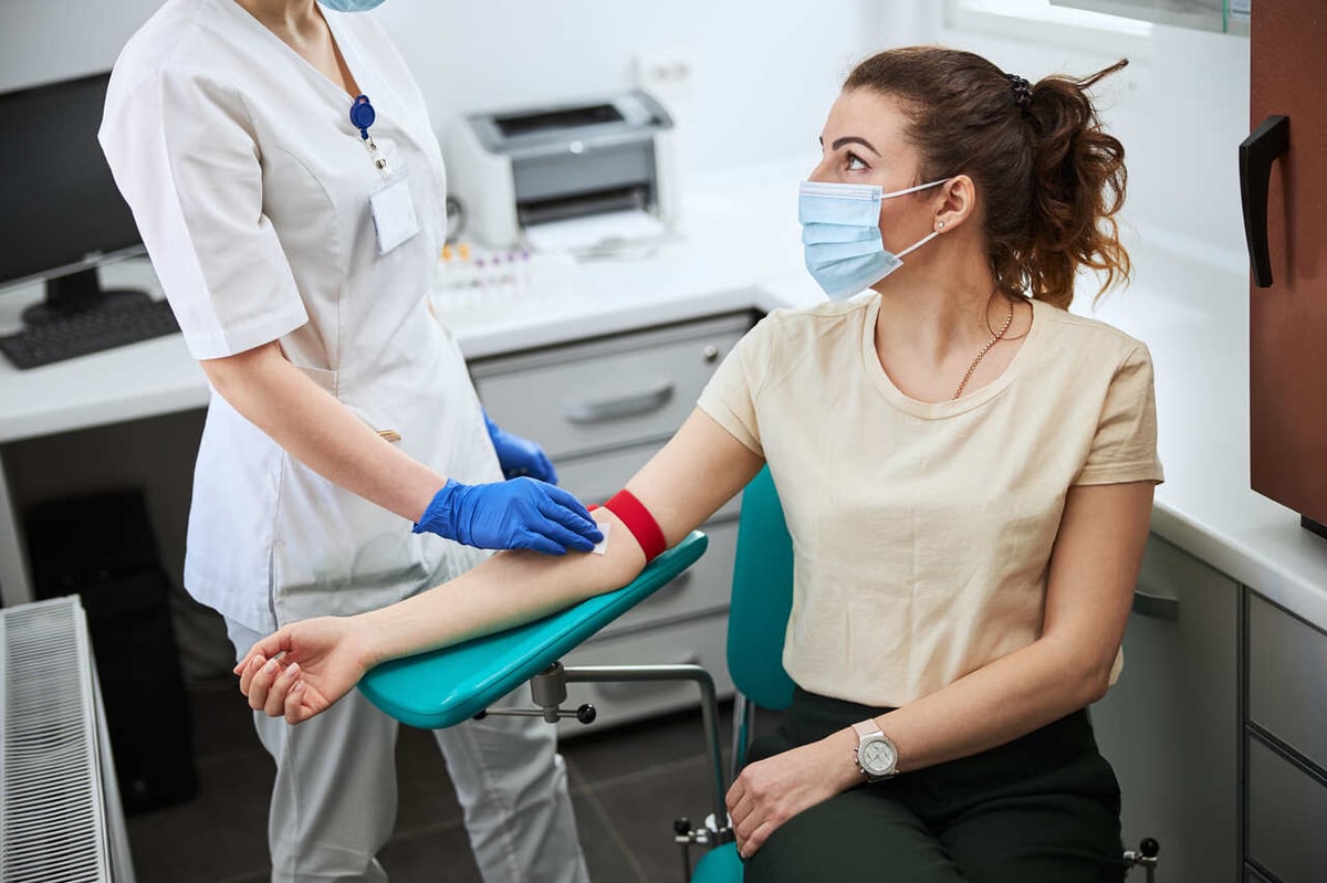 EIne Arzthelferin nimmt bei einer Frau Blut ab.