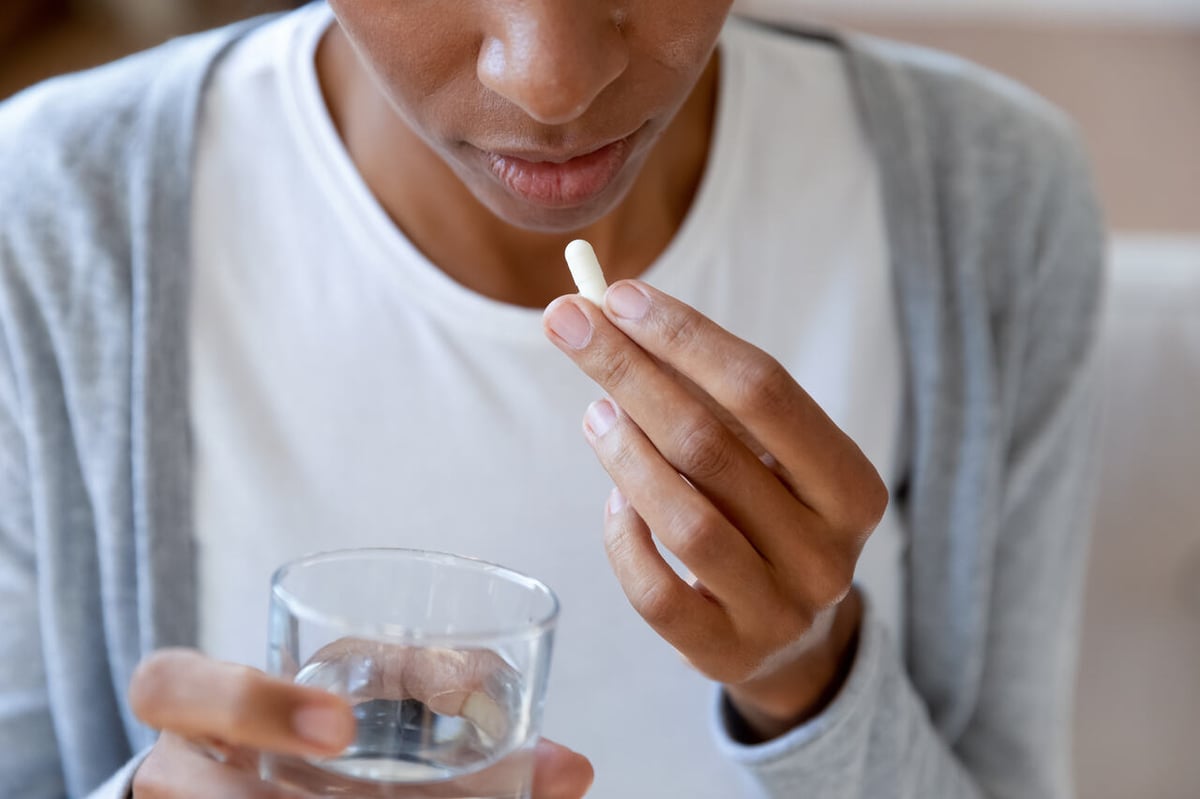 Eine Frau nimmt Antibiotika als Kapseln mit einem Glas Wasser ein.