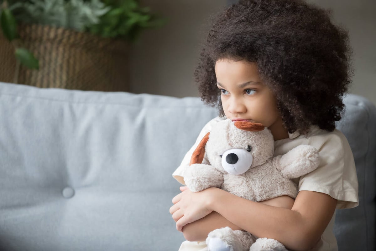 Trauriges Mädchen mit Teddybär auf Sofa.