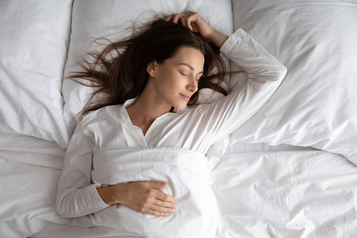 Eine Frau schläft in einem Bett mit weißen Bettbezügen.