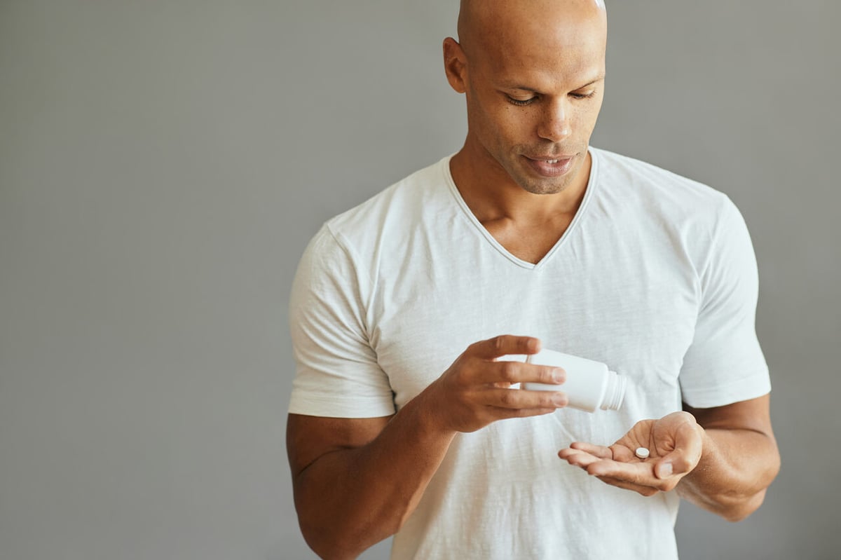 Ein junger mann mit Glatze schüttet sich Tabletten in die Hand.