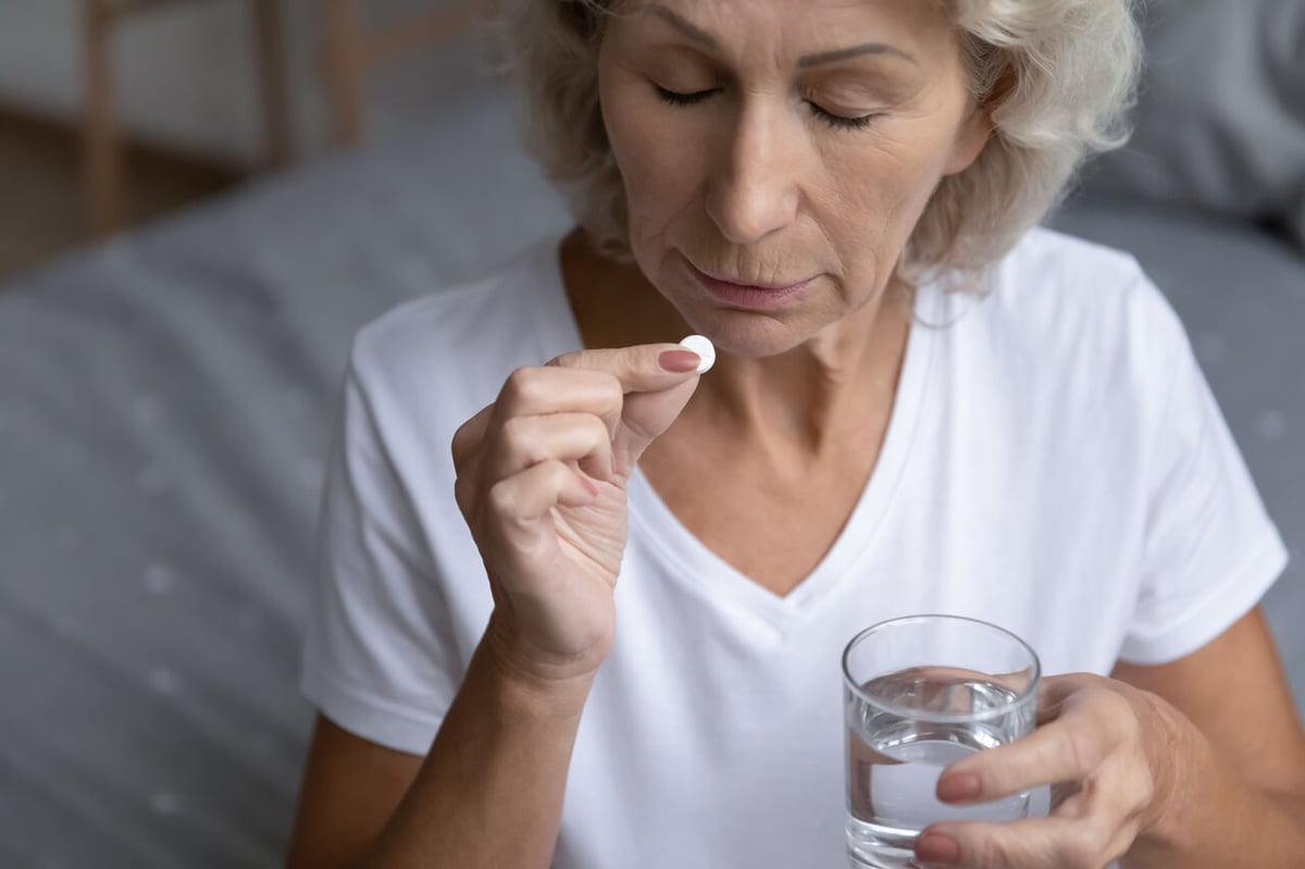 Eine Seniorin nimmt eine runde Tablette mit einem Glas Wasser ein.