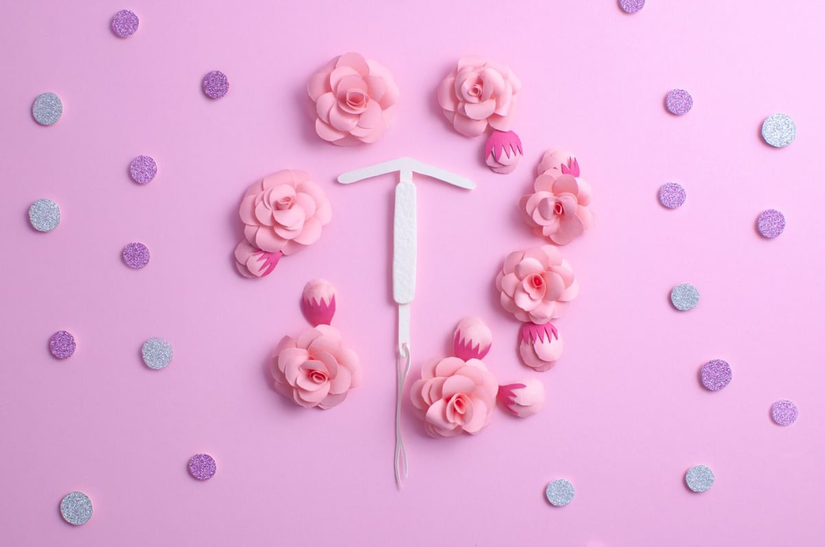 Bunte Darstellung einer Hormonspirale mit pinkem Hintergrund und Blumen.