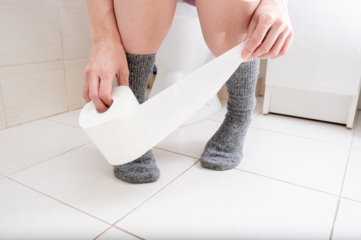 Hände greifen nach Toilettenpapier auf Toilette.