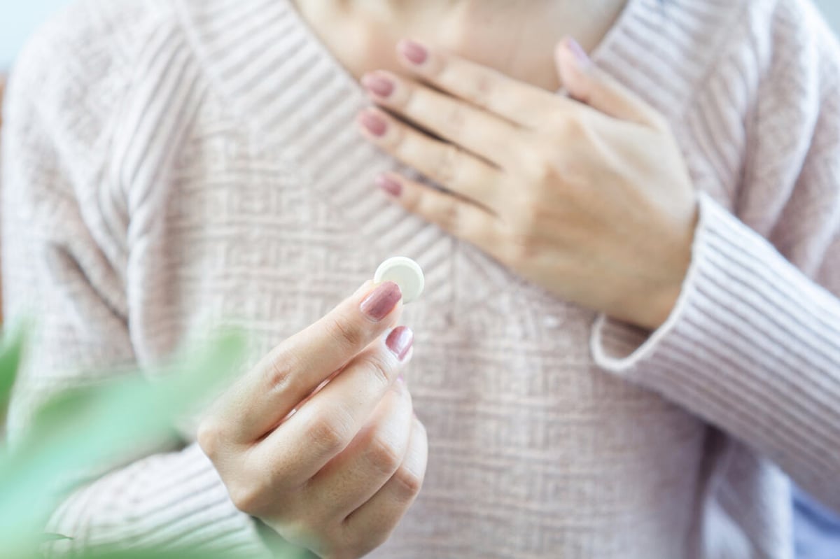 Frau hält mit der einen Hand die schmerzende Brust und in der anderen Hand eine Tablette.