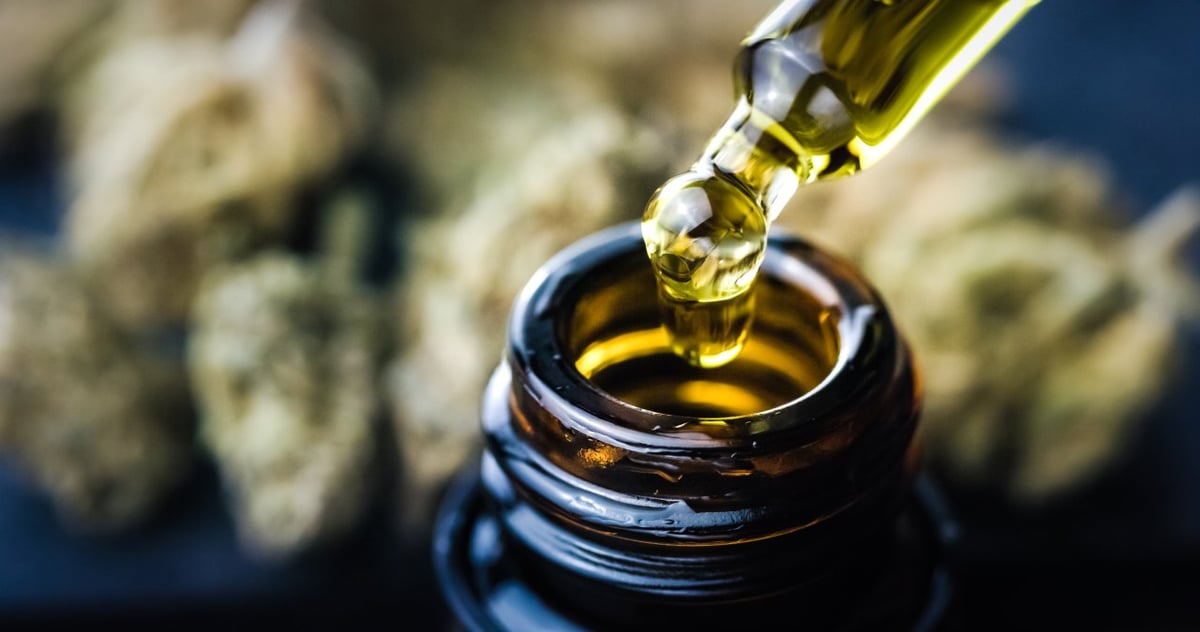 Eine Fokusaufnahme von Cannabisöl. Im Hintergrund sind Cannabisblüten zu sehen.