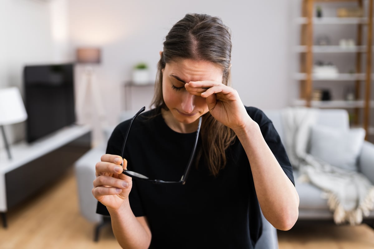 Frau am Schreibtisch hält eine Brille in der Hand und reibt sich die Augen.
