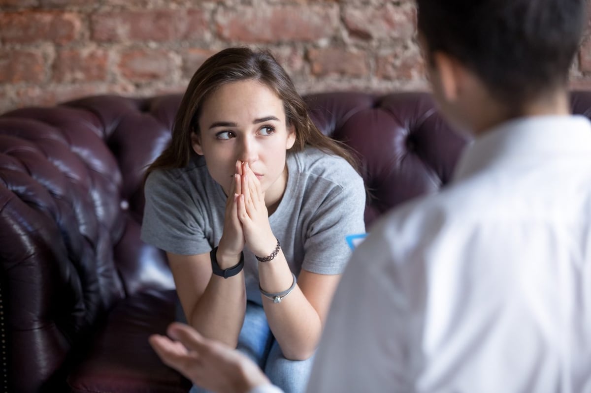 Mädchen sitzt auf einer Ledercouch, sie guckt besorgt. Vor ihr sitzt eine Psychotherapeutin.