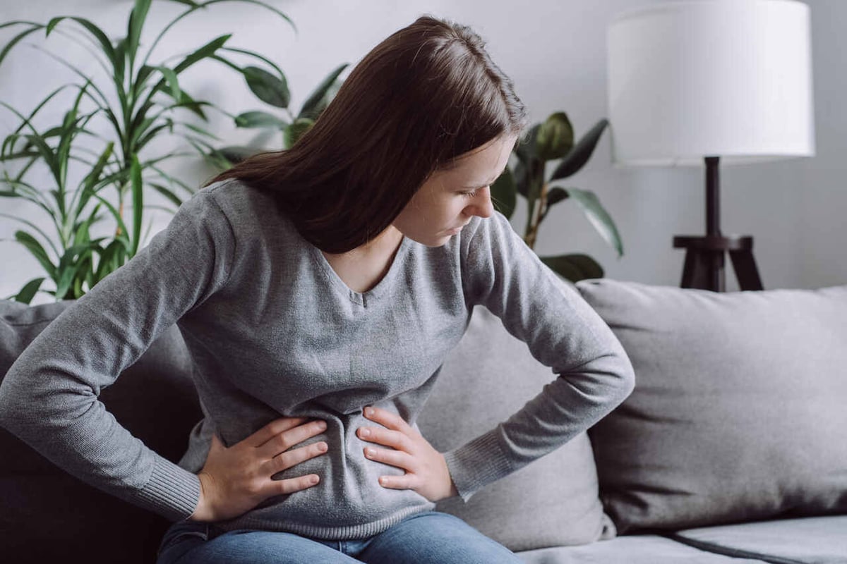 Eine junge Frau sitzt auf dem Sofa und hält sich vor Schmerzen den Bauch.