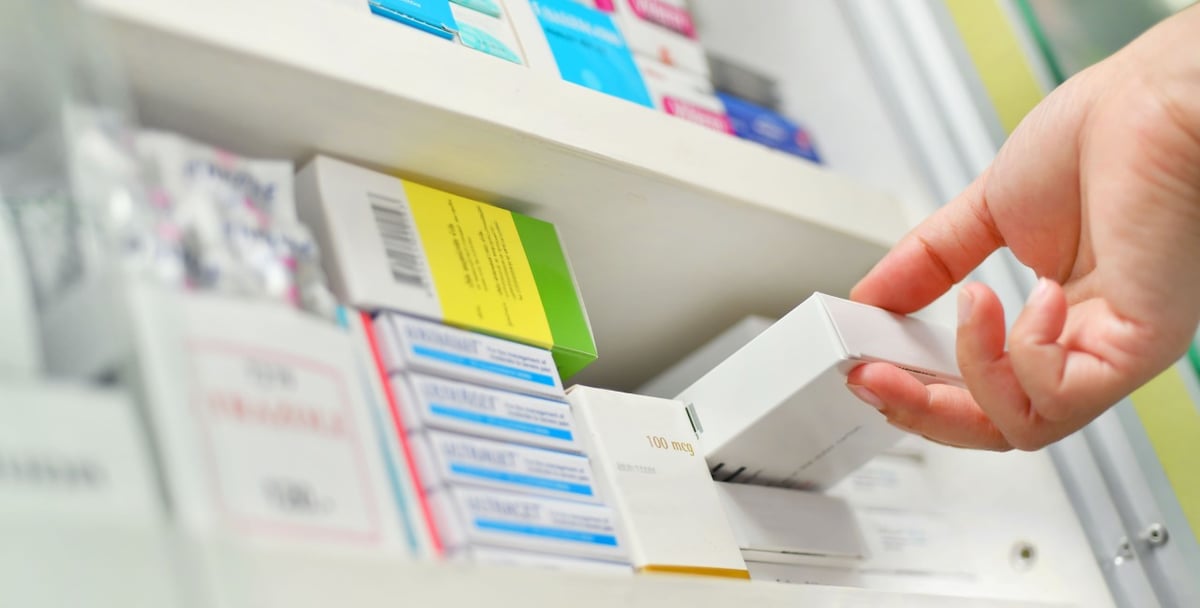 Apotheker oder Apothekerin nimmt Tabletten in Schachtel aus einem Regal.
