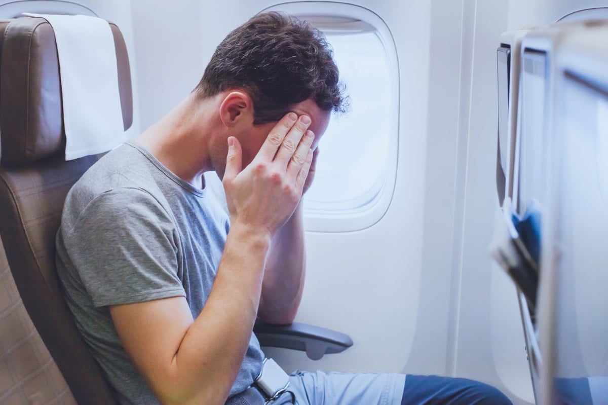 Mann sitzt im Flugzeug und hält sich die Hände vor das Gesicht.
