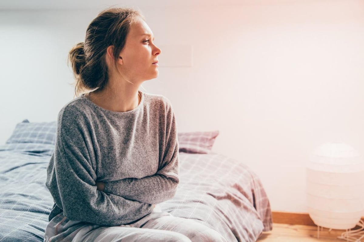 Eine Frau sitzt auf dem Bett und hält sich vor Schmerzen den Bauch.
