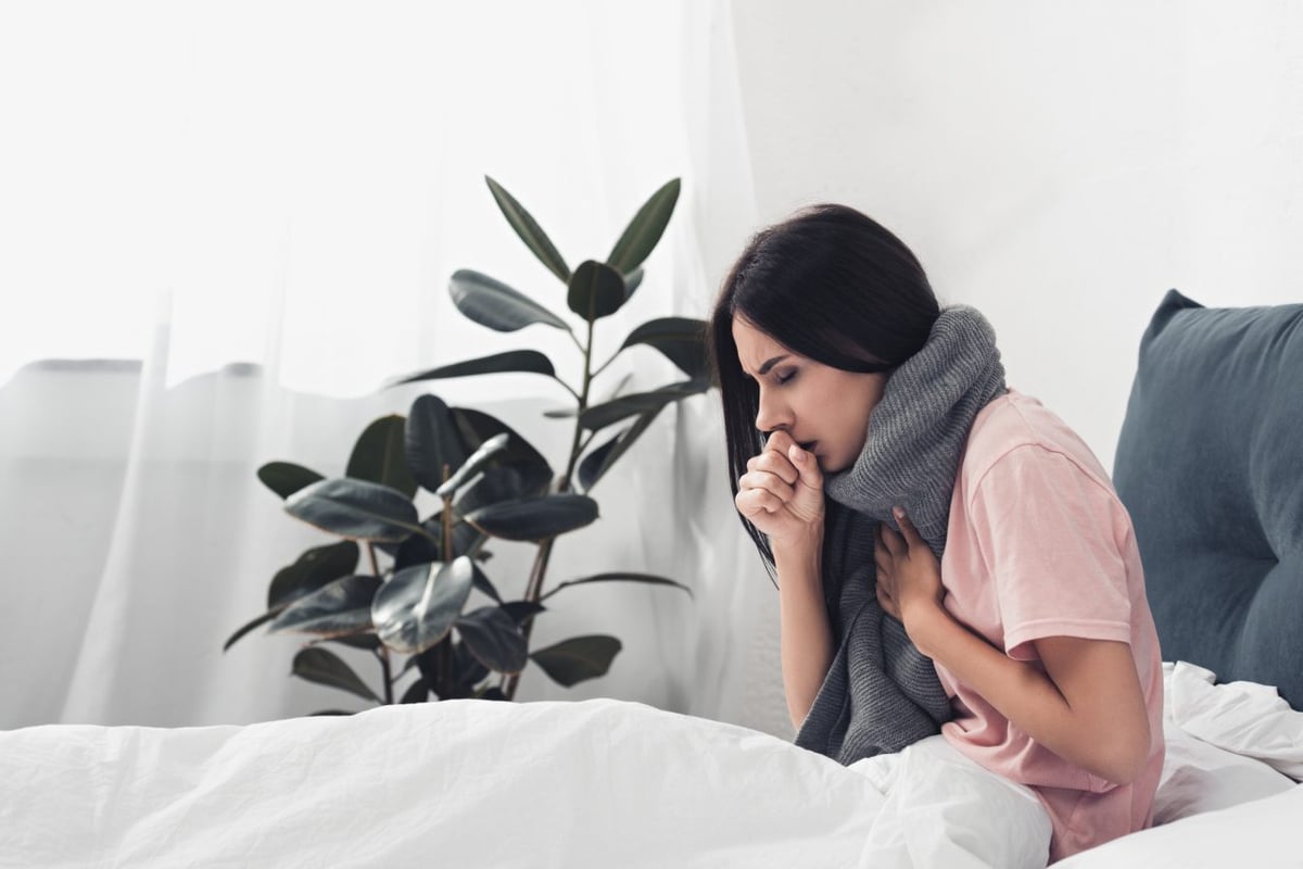 Kranke Frau sitzt im Bett und hustet.