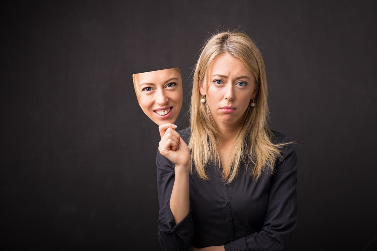 Darstellung von Depression: Traurige Frau hat eine glückliche Maske.