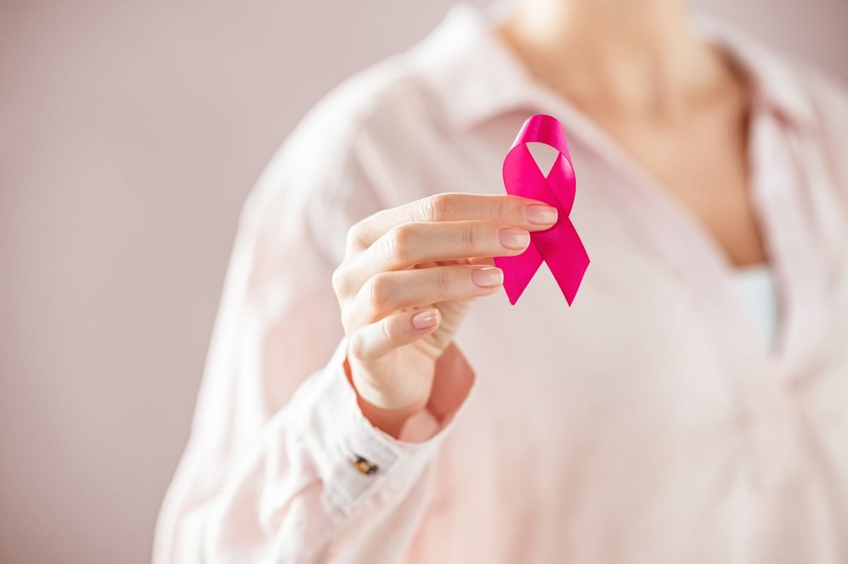 Frau hält rosa Schleife als Zeichen gegen Brustkrebs in der Hand.