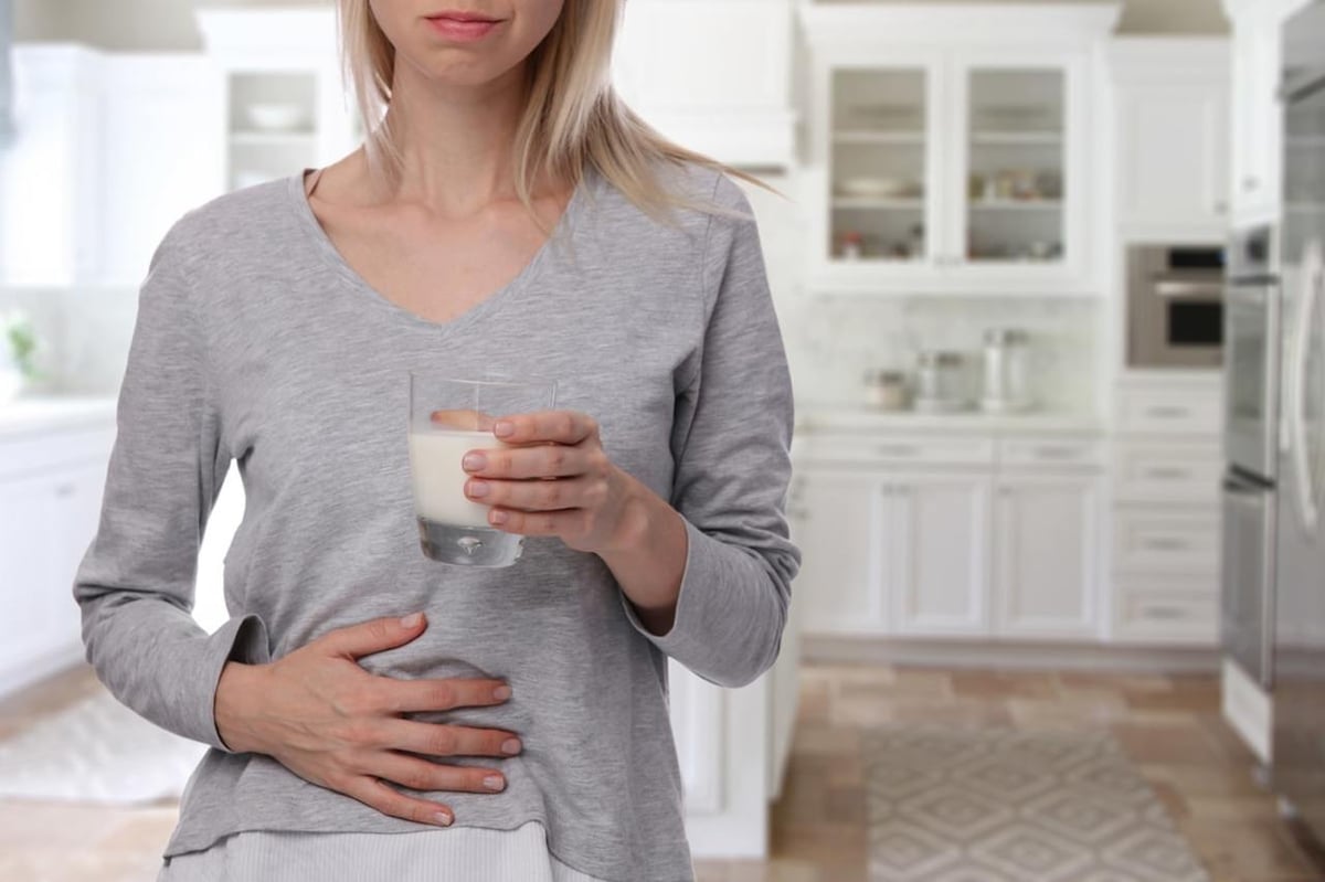 Laktoseintoleranz: Frau hält Glas mit Milch in der einen Hand, mit der anderen Hand hält sie ihren schmerzenden Bauch.