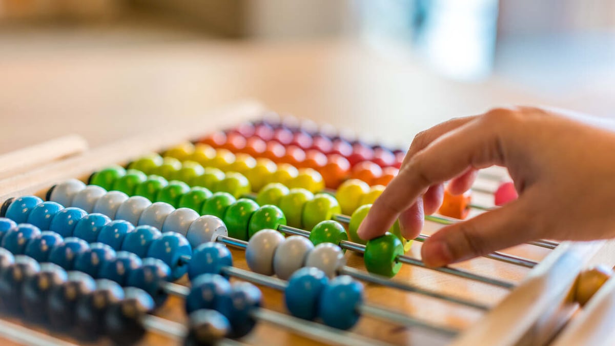 Eine Hand schiebt bunte Perlen zur Berechnung mithilfe eines Abakus hin und her.