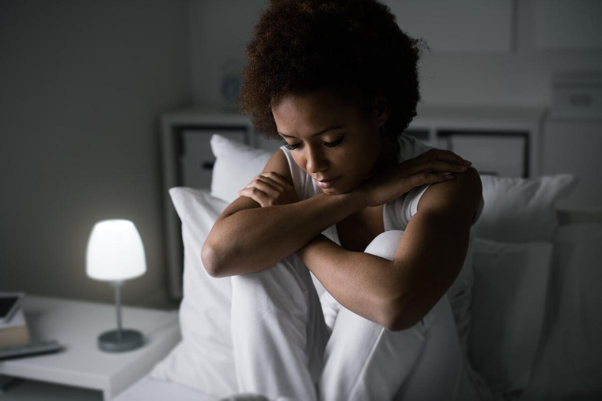 Eine junge Frau sitzt niedergeschlagen auf einem Bett.