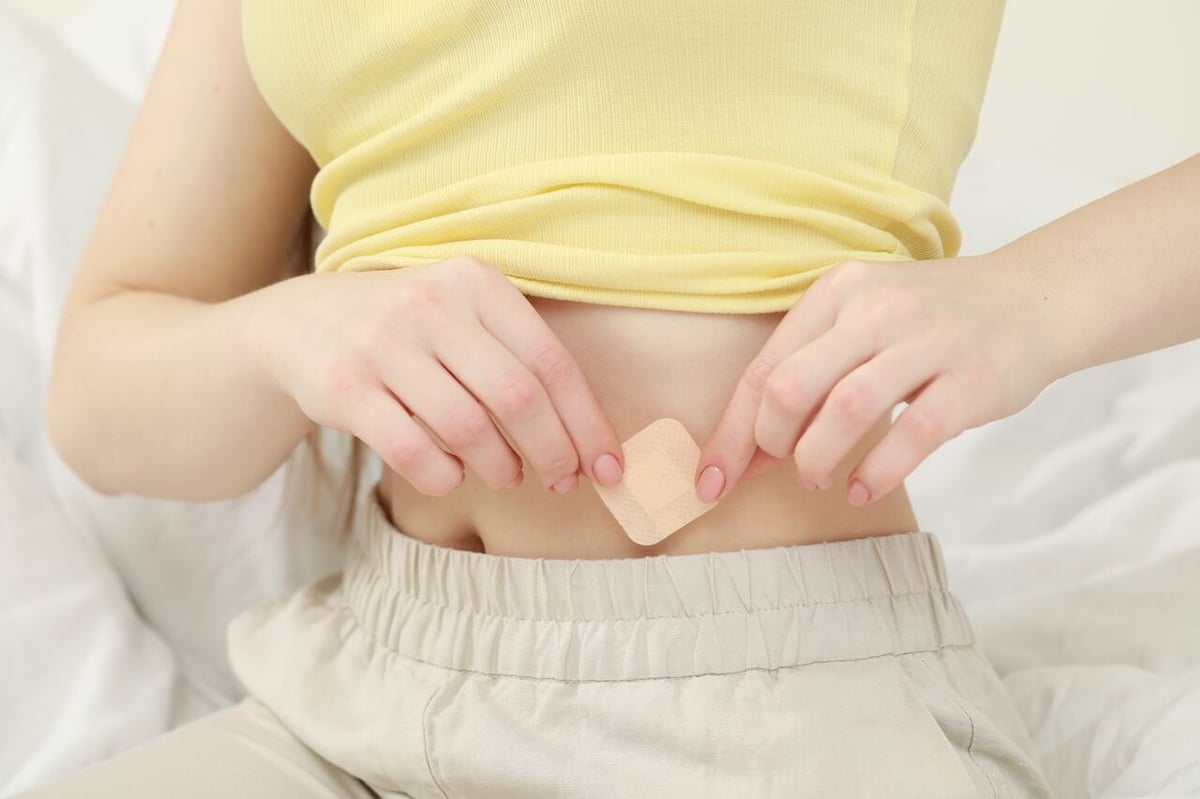Eine Frau klebt sich ein Pflaster zur Empfängnisverhütung auf den Bauch.