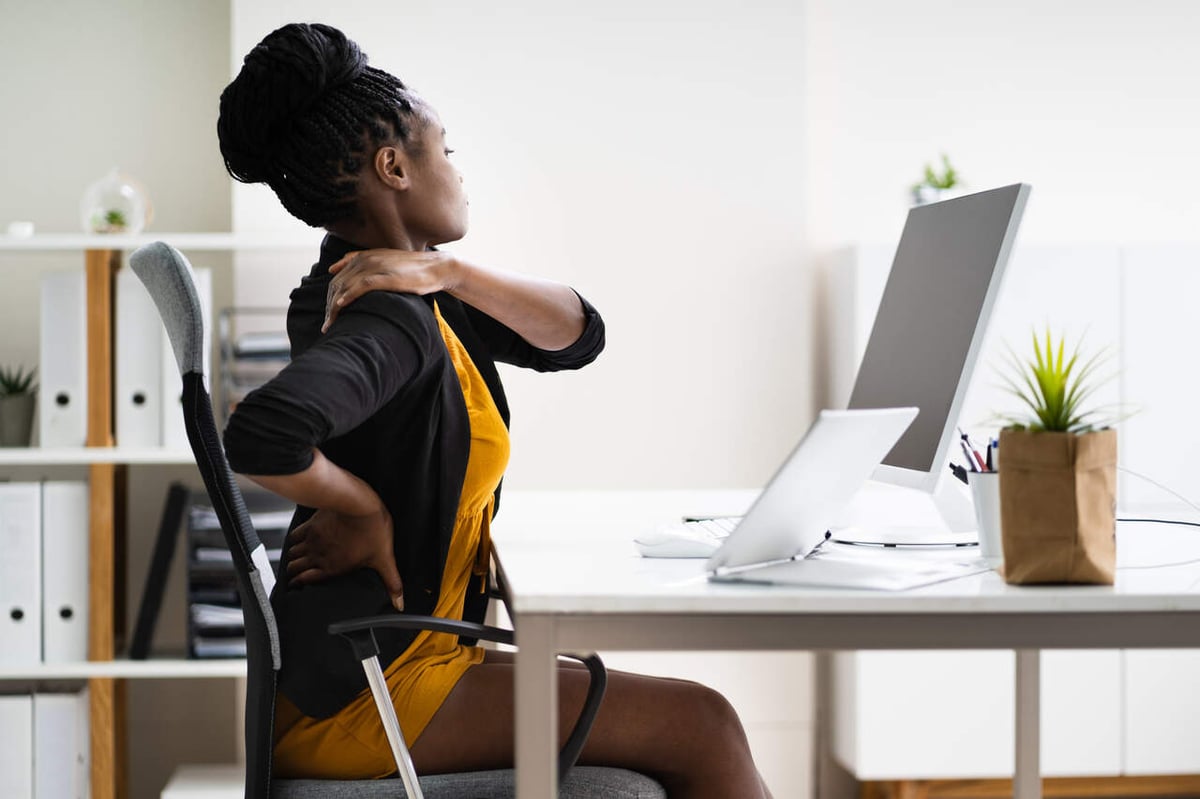 Eine Frau sitzt im Büro am Schreibtisch und hält sich den Schmerzenden Rücken.