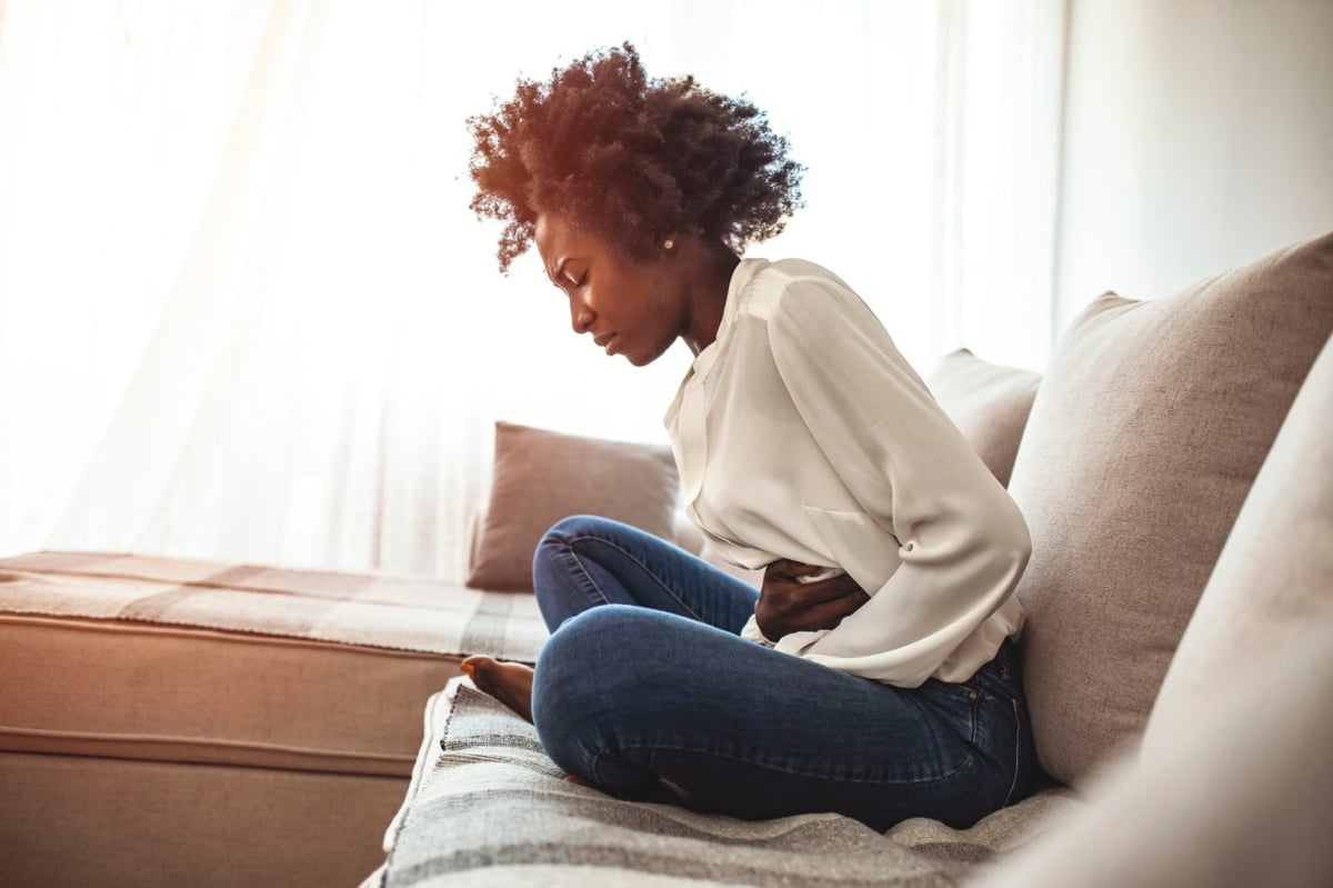 Frau mit Unterleibsschmerzen auf Sofa.